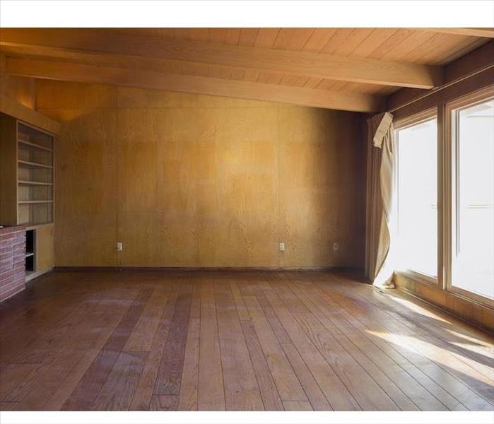 A dated upstairs living room with wood flooring, wood wall paneling, exposed wood ceiling structure, and large windows