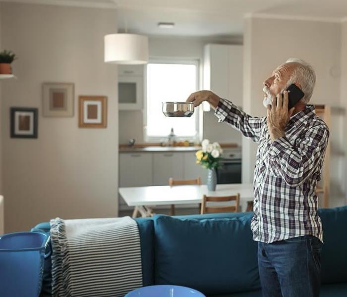 A man on the phone with a blue water bucket catching falling water.
